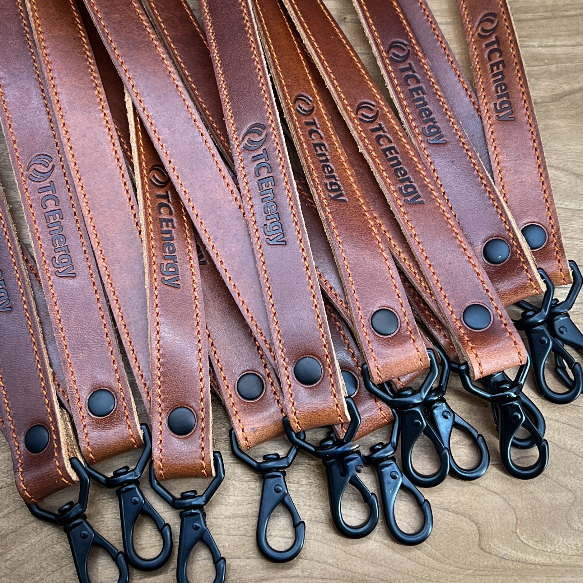 Bulk order of handmade badge lanyards in Bourbon Horween leather with orange stitching and matte black hardware.