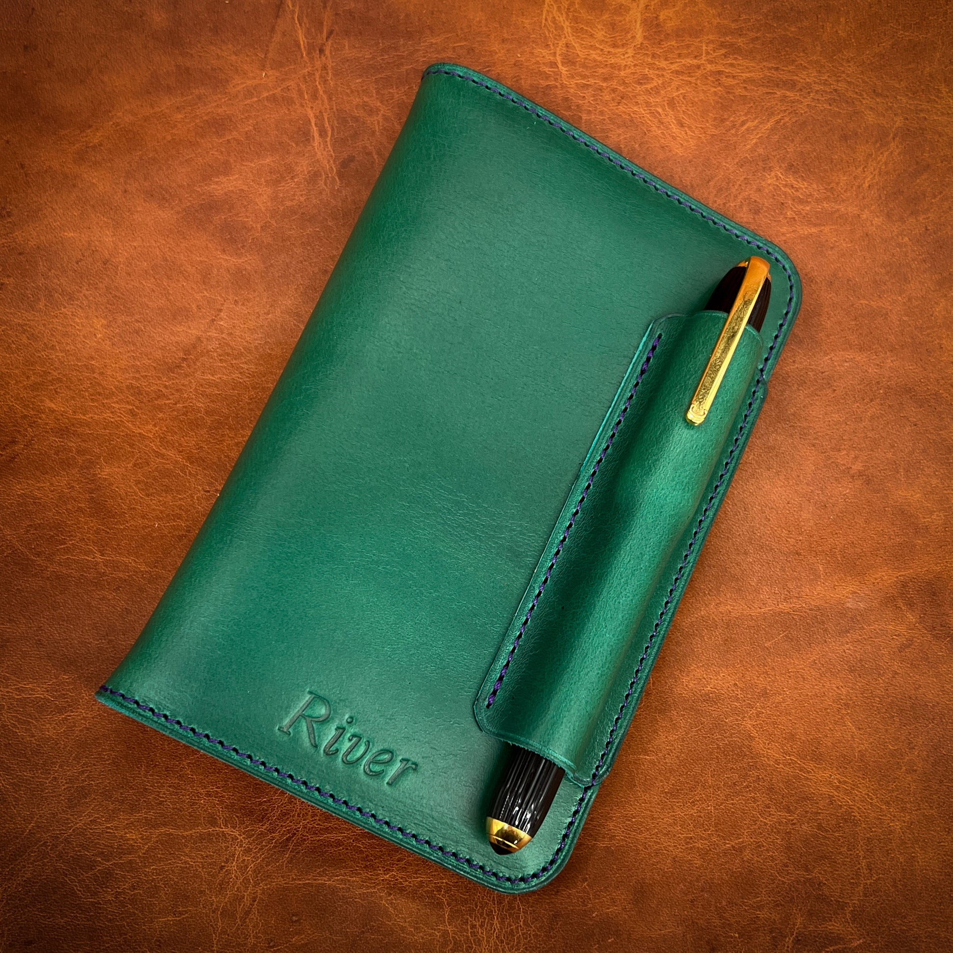 Golf Green Horween Notebook Cover with Pen Holder Stitched on the top.  Unusual Purple Accent Stitching and Cartier Pen.  Bespoke notebook cover by Custom Leather and Pen in Houston, TX